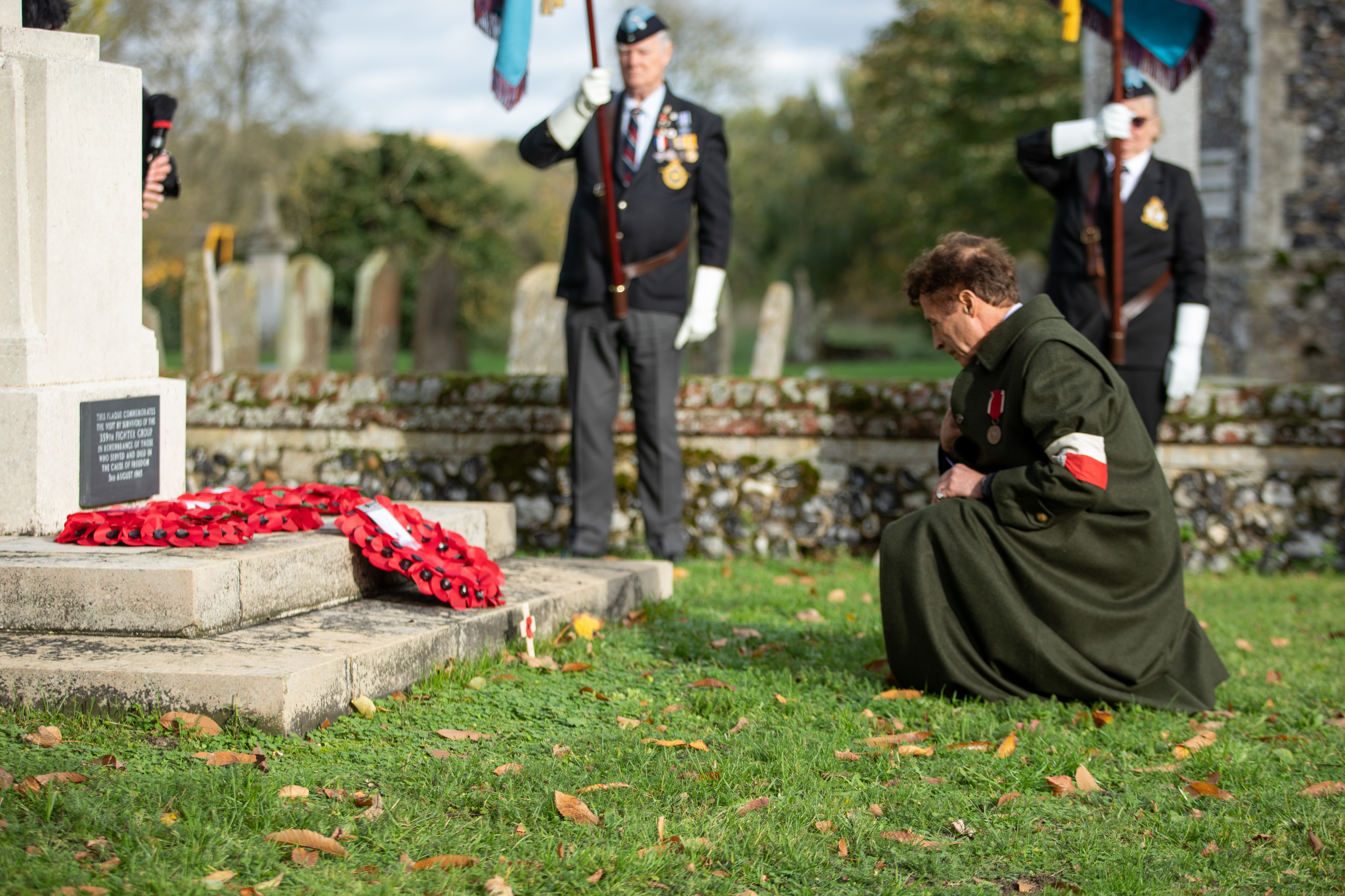 Image shows RAF aviator kneeling before memorial with poppy wreath.